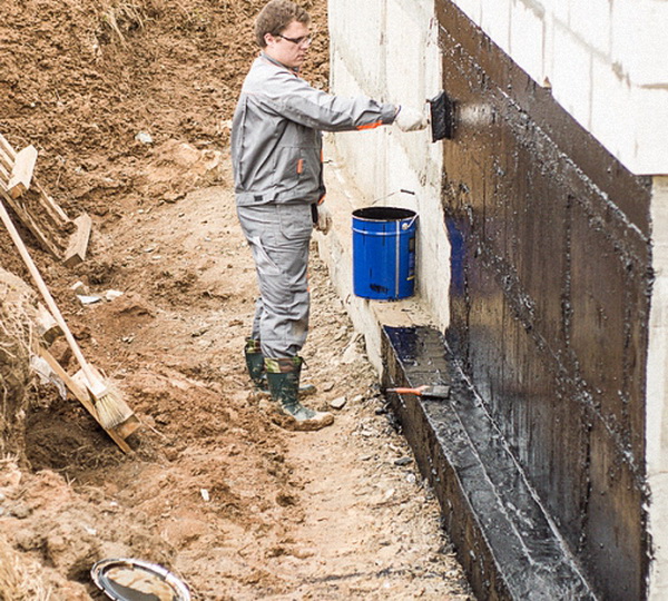 Рабочий покрывает стену праймером